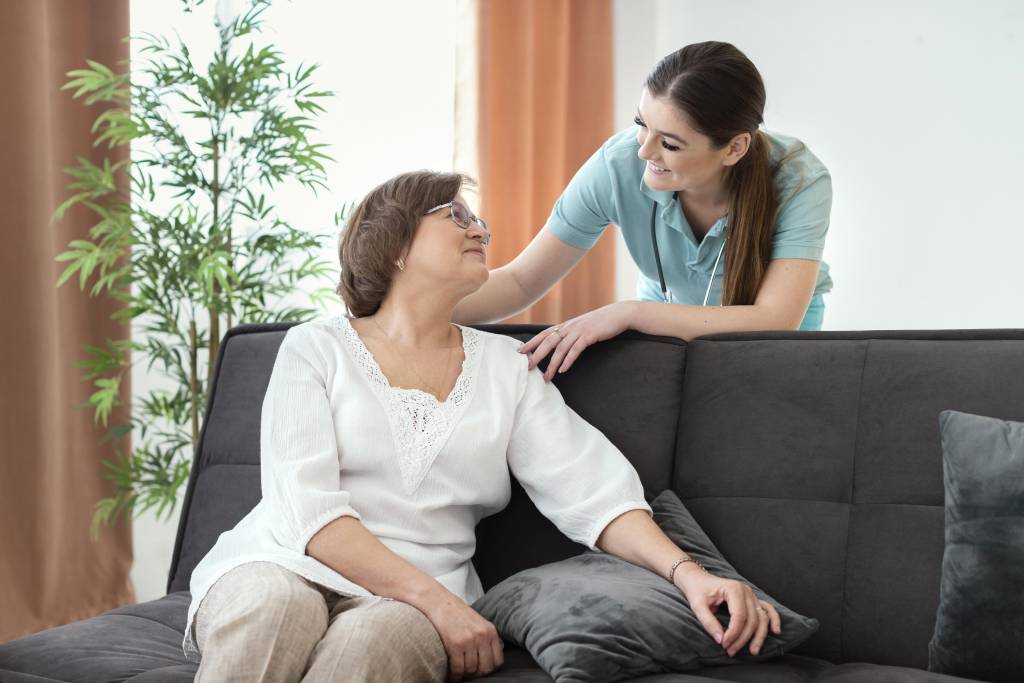 Women sharing a caring moment on a couch, representing in-home massage therapy for seniors, emphasizing comfort and connection in a relaxed setting.
